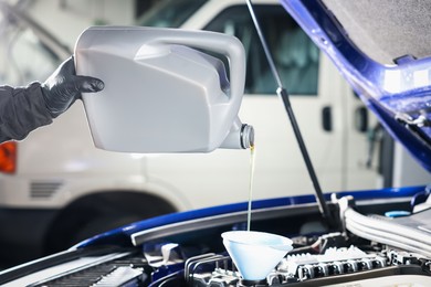 Photo of Worker pouring motor oil from canister into car engine, closeup