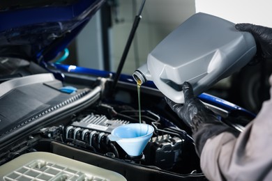 Photo of Worker pouring motor oil from canister into car engine, closeup