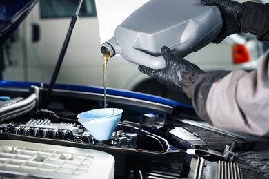 Photo of Worker pouring motor oil from canister into car engine, closeup