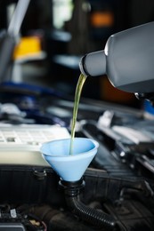 Photo of Pouring motor oil from bottle into car engine, closeup