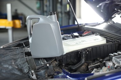 Photo of Canister of motor oil on car engine in workshop, closeup