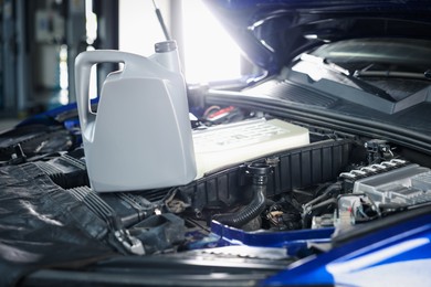 Photo of Canister of motor oil on car engine in workshop, closeup