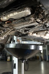 Photo of Dirty old motor oil dripping from car engine into container in workshop, closeup