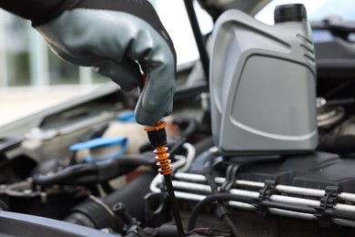Photo of Worker checking motor oil level in car with dipstick, closeup