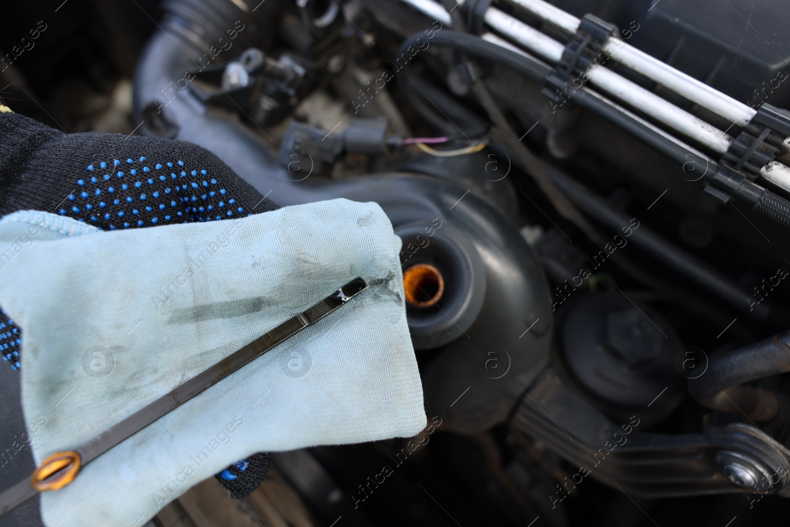 Photo of Worker checking motor oil level in car with dipstick, closeup