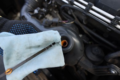 Photo of Worker checking motor oil level in car with dipstick, closeup