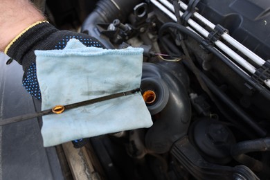 Photo of Worker checking motor oil level in car with dipstick, closeup