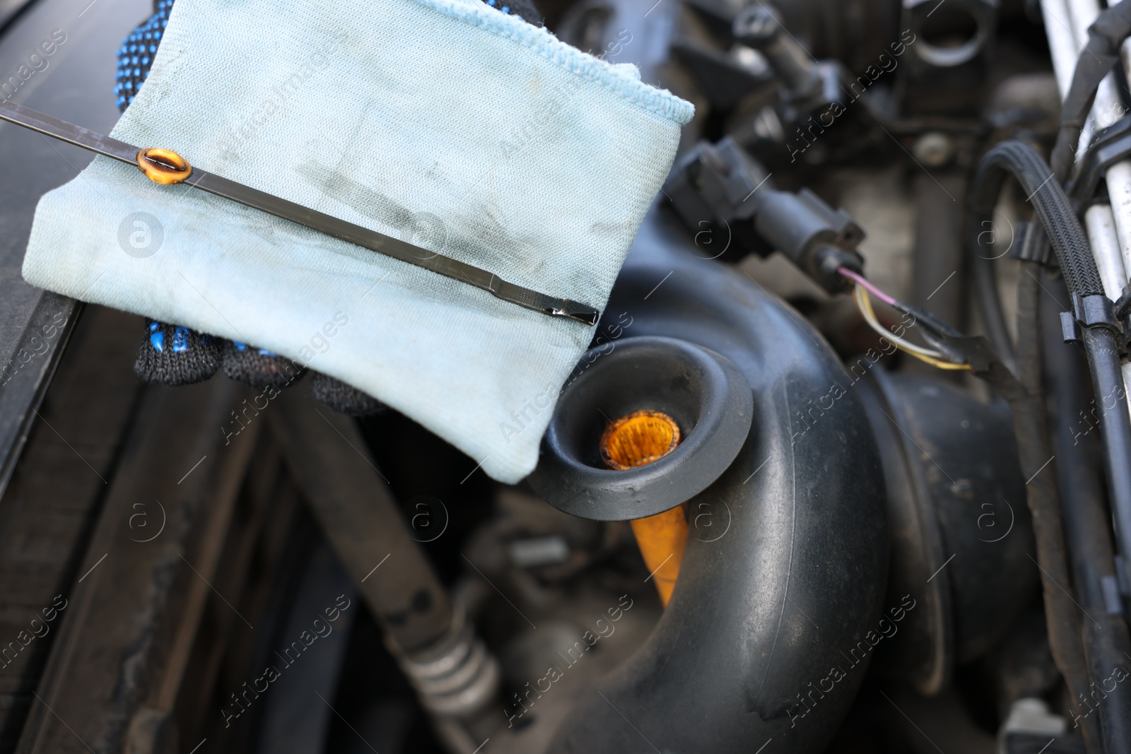 Photo of Worker checking motor oil level in car with dipstick, closeup