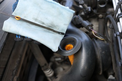 Photo of Worker checking motor oil level in car with dipstick, closeup