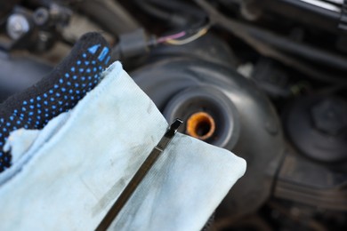 Photo of Worker checking motor oil level in car with dipstick, closeup