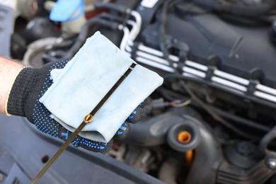 Photo of Worker checking motor oil level in car with dipstick, closeup