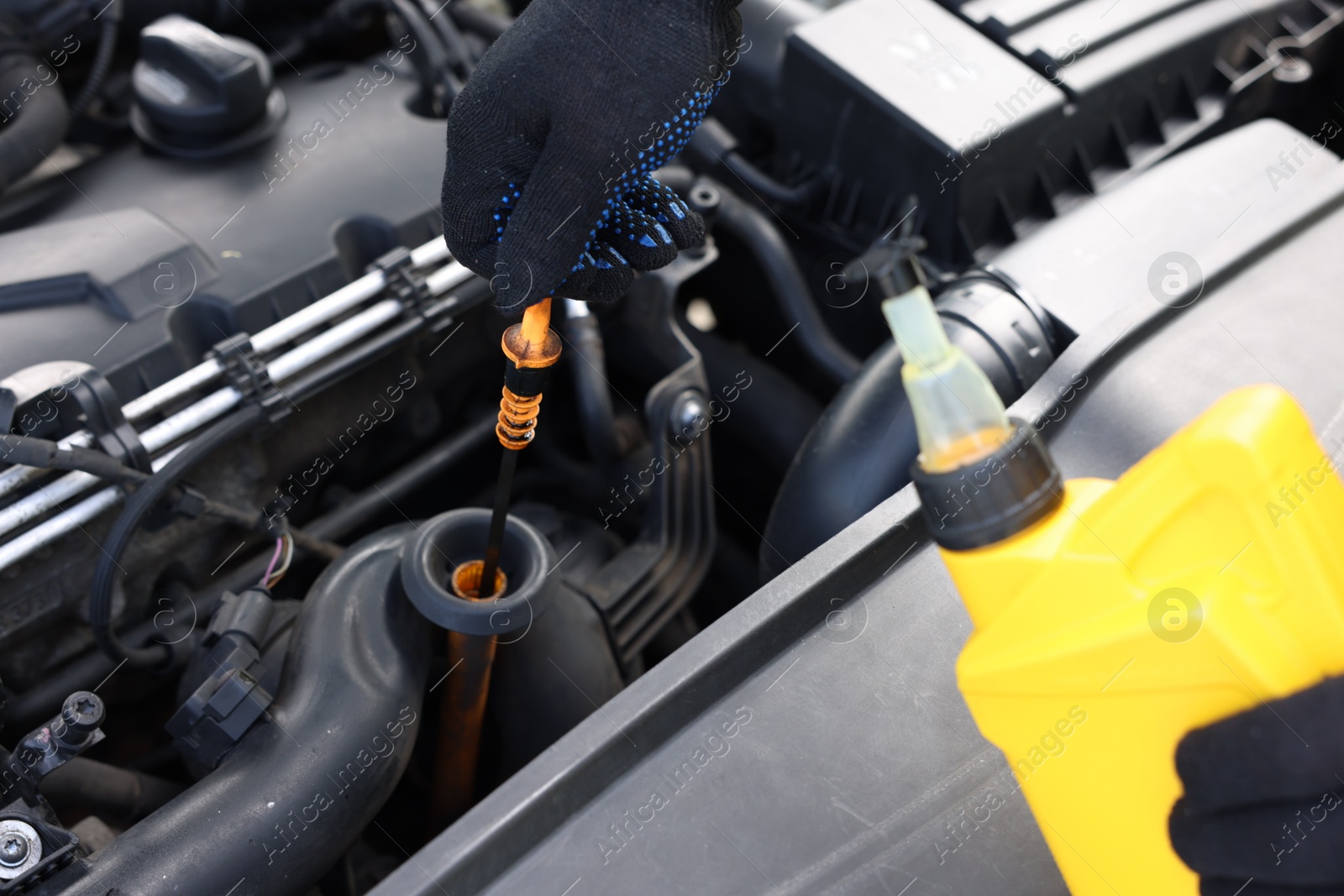 Photo of Worker checking motor oil level in car with dipstick, closeup