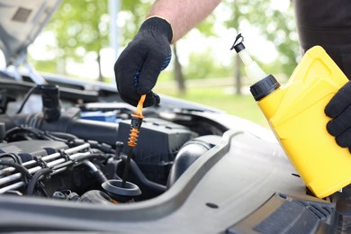 Photo of Worker checking motor oil level in car with dipstick, closeup