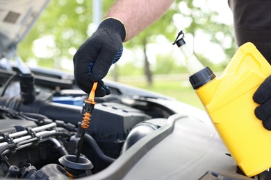 Photo of Worker checking motor oil level in car with dipstick, closeup