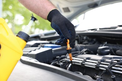 Photo of Worker checking motor oil level in car with dipstick, closeup