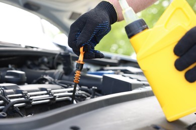Photo of Worker checking motor oil level in car with dipstick, closeup