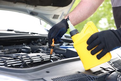 Photo of Worker checking motor oil level in car with dipstick, closeup