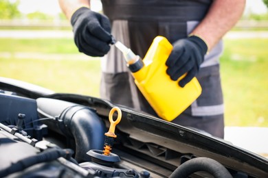 Photo of Worker checking motor oil level in car with dipstick, closeup