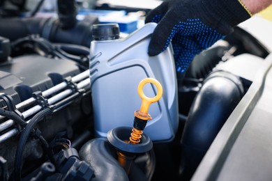 Photo of Worker checking motor oil level in car with dipstick, closeup
