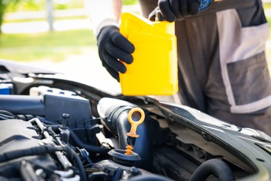 Photo of Worker checking motor oil level in car with dipstick, closeup
