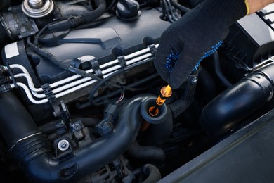 Photo of Worker checking motor oil level in car with dipstick, closeup