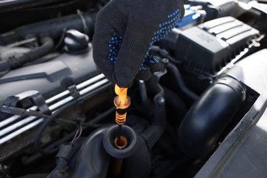 Photo of Worker checking motor oil level in car with dipstick, closeup