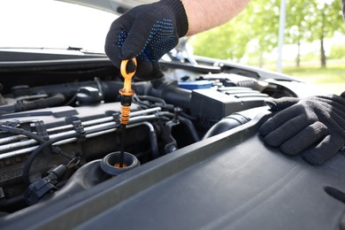 Photo of Worker checking motor oil level in car with dipstick, closeup