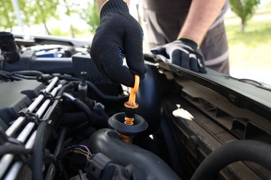 Photo of Worker checking motor oil level in car with dipstick, closeup