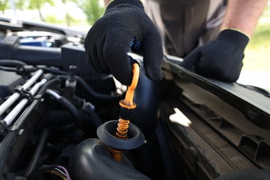 Photo of Worker checking motor oil level in car with dipstick, closeup