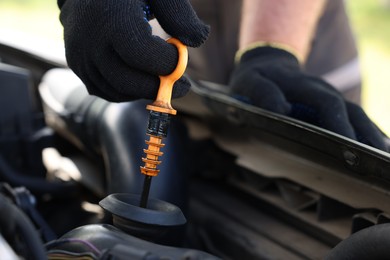 Photo of Worker checking motor oil level in car with dipstick, closeup