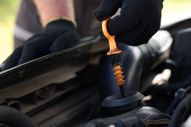 Photo of Worker checking motor oil level in car with dipstick, closeup