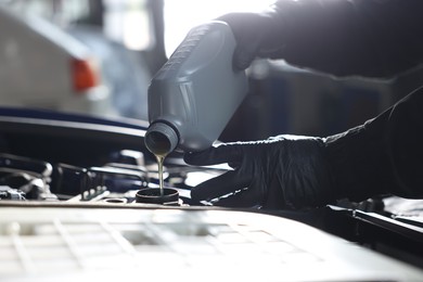 Photo of Worker pouring motor oil from canister into car engine, closeup