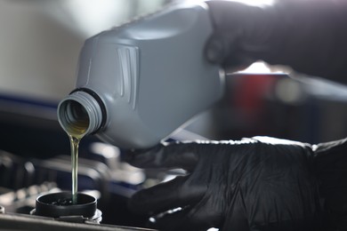 Photo of Worker pouring motor oil from canister into car engine, closeup