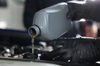 Photo of Worker pouring motor oil from canister into car engine, closeup