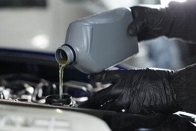 Photo of Worker pouring motor oil from canister into car engine, closeup
