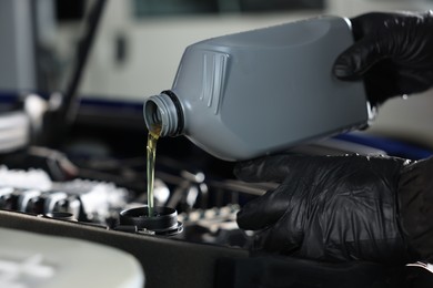Photo of Worker pouring motor oil from canister into car engine, closeup