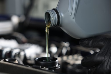 Photo of Pouring motor oil from bottle into car engine, closeup