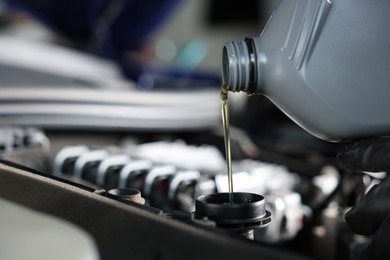 Photo of Pouring motor oil from bottle into car engine, closeup