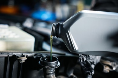 Photo of Pouring motor oil from bottle into car engine, closeup