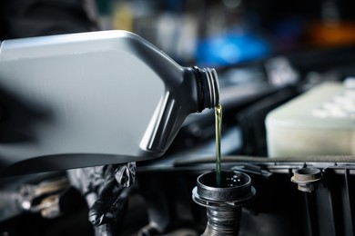 Photo of Pouring motor oil from bottle into car engine, closeup