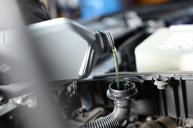 Photo of Pouring motor oil from bottle into car engine, closeup