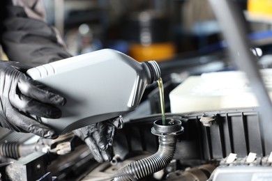 Photo of Worker pouring motor oil from canister into car engine, closeup