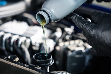 Photo of Worker pouring motor oil from bottle into car engine, closeup