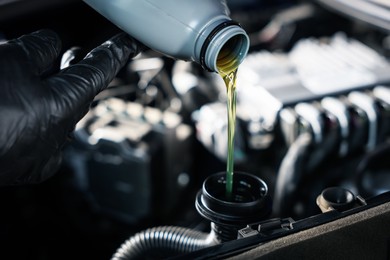 Photo of Worker pouring motor oil from bottle into car engine, closeup