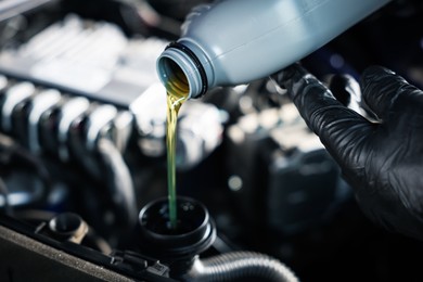 Photo of Worker pouring motor oil from bottle into car engine, closeup