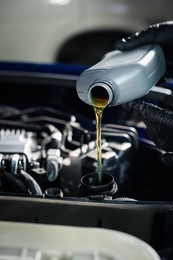 Photo of Worker pouring motor oil from bottle into car engine, closeup