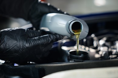 Photo of Worker pouring motor oil from bottle into car engine, closeup