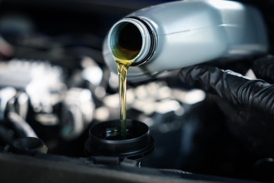 Photo of Worker pouring motor oil from canister into car engine, closeup
