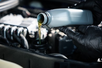 Photo of Worker pouring motor oil from canister into car engine, closeup