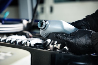 Photo of Worker pouring motor oil from canister into car engine, closeup